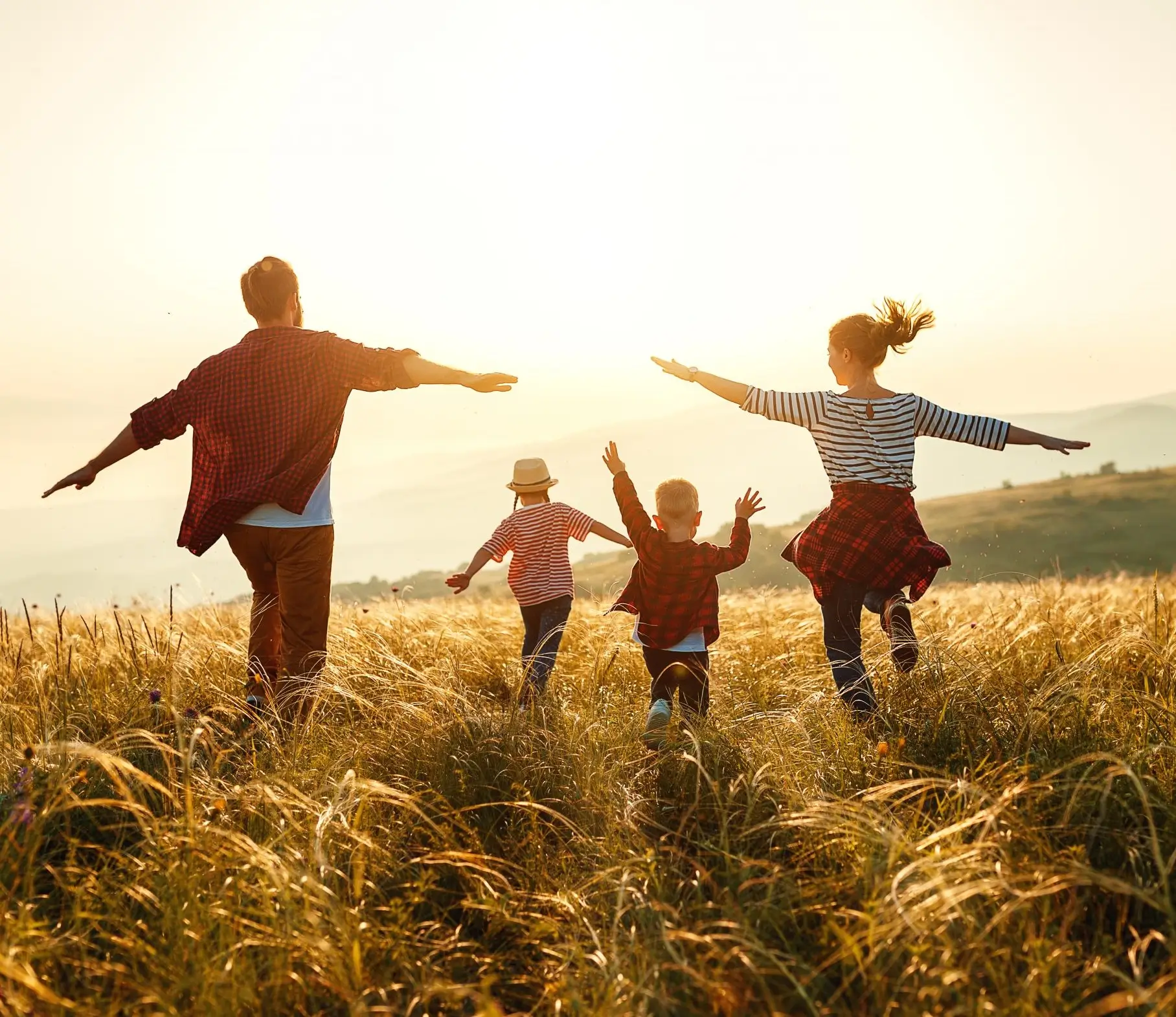 A family is running through the grass in the sun.